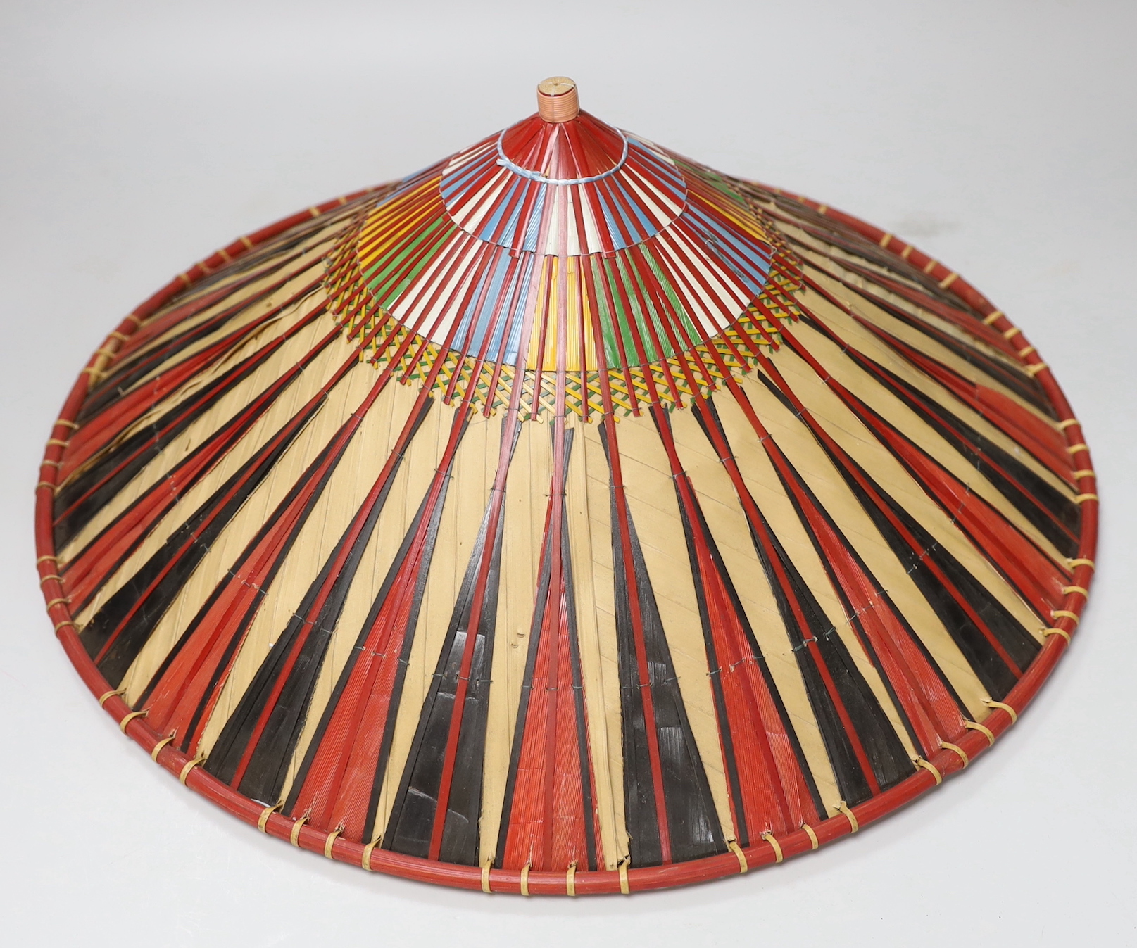 Three red and black striped bamboo rice hats, together with a smaller rice hat with beaded flag decoration